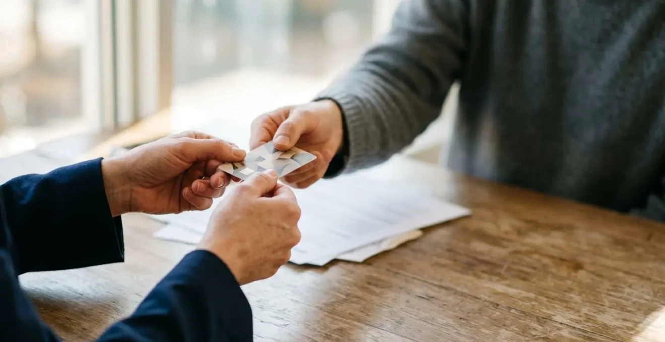 Vue rapprochée de mains échangeant une carte de crédit dans un contexte professionnel avec documents contractuels flous en arrière-plan